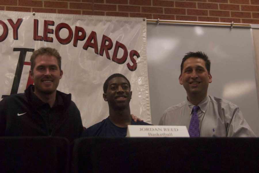 Signing a Letter of Intent to accept attend Rice on a scholarship, senior Jordan Reed shares the stage with assistant basketball coach Justin Kauffman (on left) and head coach Kyle Herema (on right).  Reed is one of three students to sign with a Division I school.