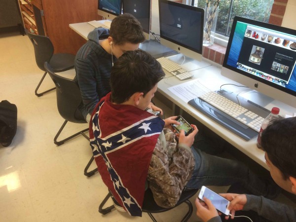 With the Confederate flag draped over his shoulders, freshman Hunter George looks at his phone in class.