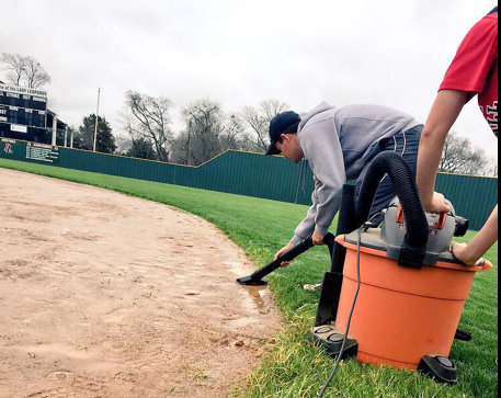 Due to increased rainfall, head softball coach Jeff Roberts vacuums up water on the fields before softball practice.  