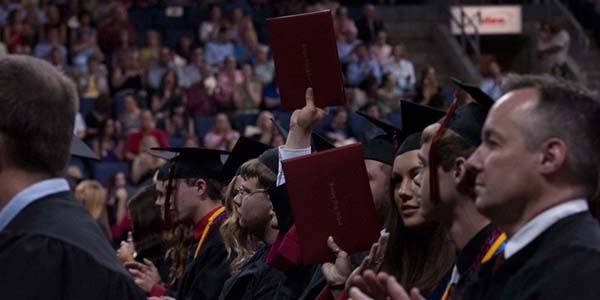 With the crowd applauding, some 2014 graduates raise their diplomas.