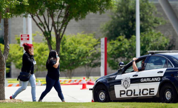 A Garland police officer directs Naaman Forest High School students around the crime scene outside the Curtis Culwell Center on Monday, May 4, 2015, the day after two gunmen armed with assault rifles and wearing body armor opened fire on an unarmed Garland ISD security guard in Garland, Texas, Sunday night. After seeing what happened, a Garland police officer shot and killed the two suspects.