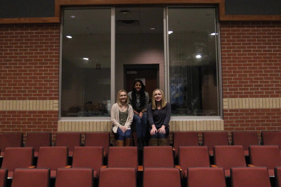 Three stage managers from recent shows, sophomore Mason Taylor Long, senior Sonali Mehta, and sophomore Lauren Latour, sit on the edge of the sound and light booth looking towards the stage.