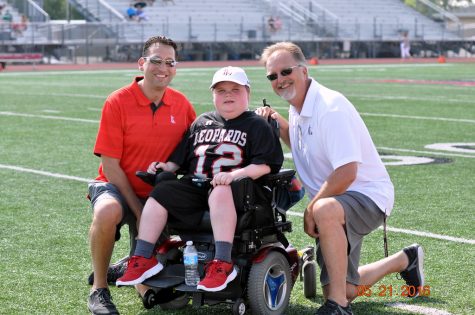 Assistant Athletic Director Kyle Herrema and Head Athletic Director Jim Bob Puckett kneels around Reed on the field at Leopard Stadium.