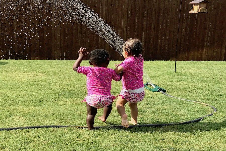 Faith Olsen and the child being adopted play in a sprinkler.