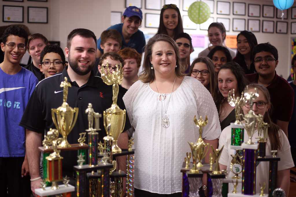 Tami Parker, Jake Cosio and the Debate I students gather around the Debate team's trophies. Parker will retire in June at the school year's end.