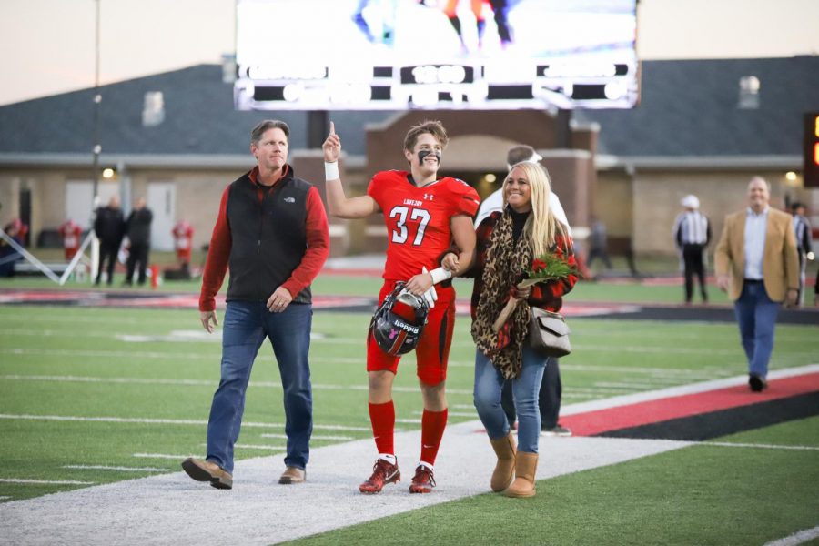 Before the game, seniors who participate in football, sports medicine, band, majestics, cross country, golf, and swim walked across the field as their names were announced on senior night. Senior football athlete Quinn McDermott walks with his parents across the field. 
