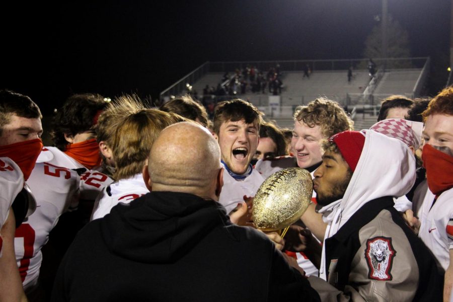 Junior running back Noah Naidoo kisses the district championship trophy while his team celebrates behind him. Naidoo suffered a jaw injury in a game against Rockhill but expects to be back on Friday. 