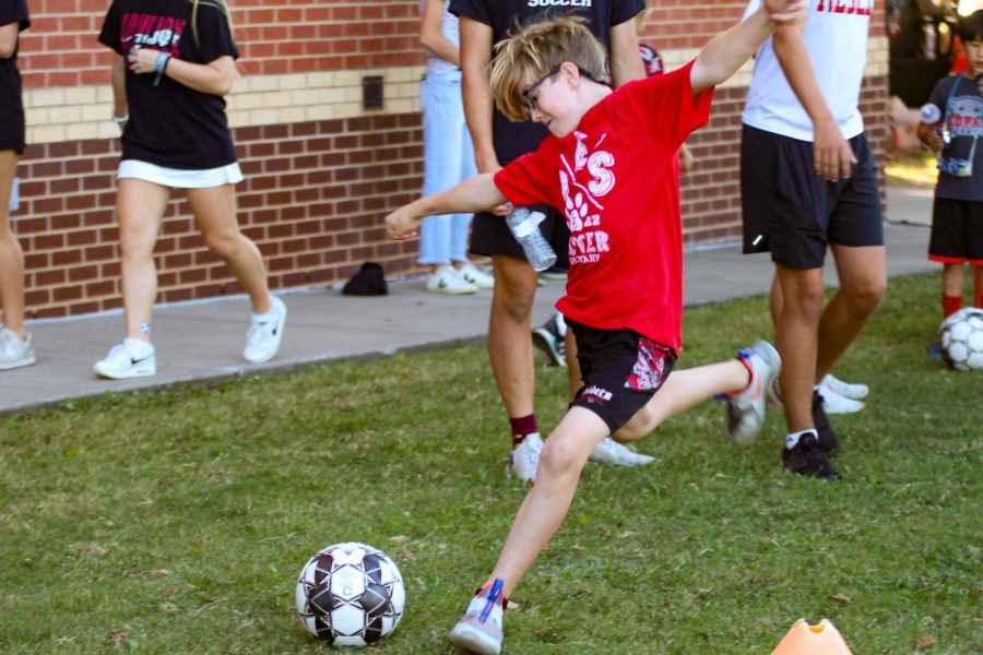 A young boy kicks a soccer ball at the boys soccer booth at Leopard Friday. He had to perform a drill that involved dribbling between cones, and then shooting the ball.