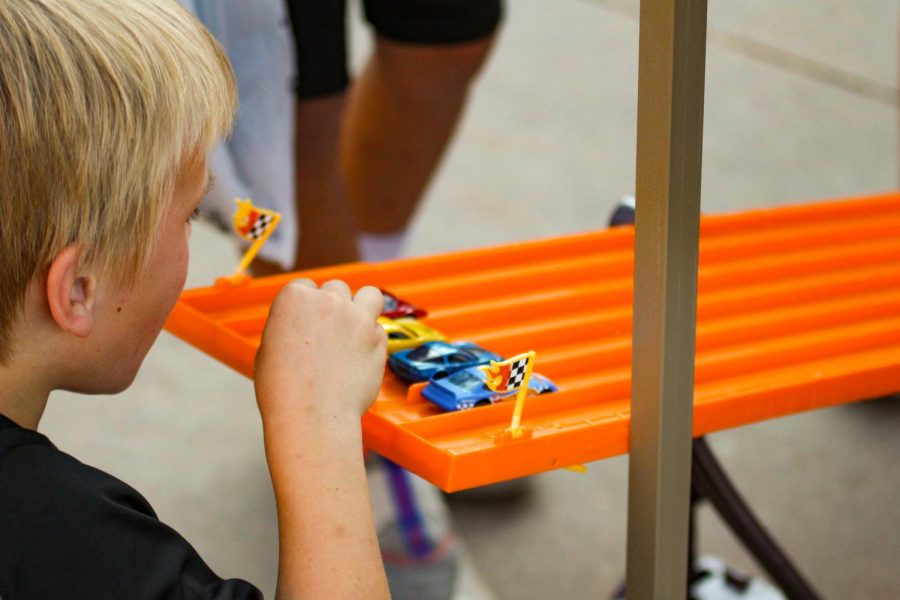 A young boy sets up cars to get ready to start a race. This was a part of the booth set up by the automotive club.