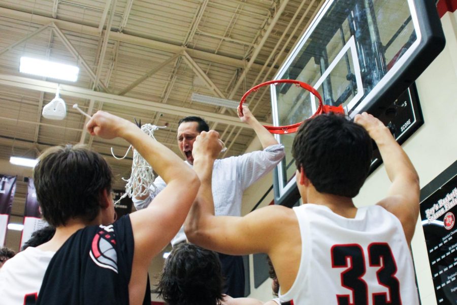 Head basketball coach Kyle Herrema celebrates the team with the net. Each team member got to cut a piece of the net after winning the game to celebrate their district title.