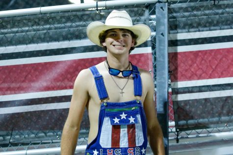 Senior Owen Cazad stands by the bleachers in his overalls for the picture. Cazad joined the dirty drumline to feel connected to the game and get into school spirit.