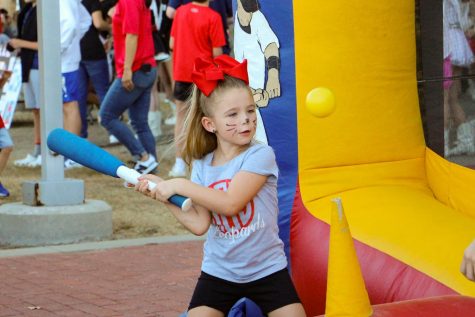A young girl swings a bat at the softball booth. The game was to try and hit a ball into different holes. 