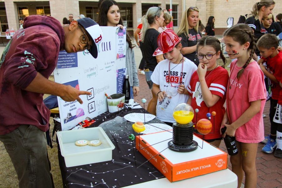 A high school student shows kids the movement of planets at the cosmic club booth. The booths took place before the football game against Poteet.