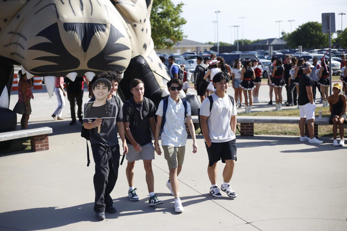 A group of senior boys walk through the courtyard. The boys are carrying a cardboard face cut out with them.