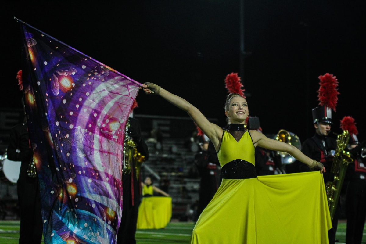 Freshman Emily Syzmanski performs with the color guard during the halftime performance. The color guard is dressed as fireflies for the performance Glow.