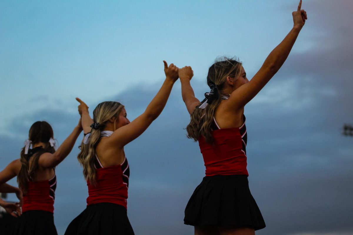 The varsity cheer team link pinkies anticipating kickoff. The team was playing Greenville.